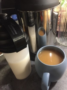 A cup of white tea with a container of oat milk next to it